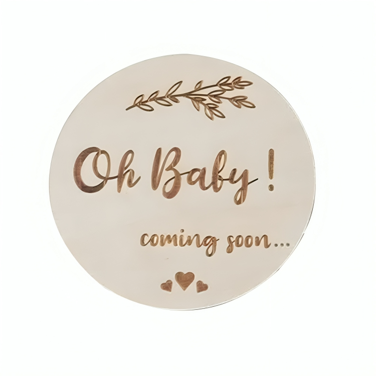 Round plaque with Oh Baby! coming soon... text and decorative leaves in a white background