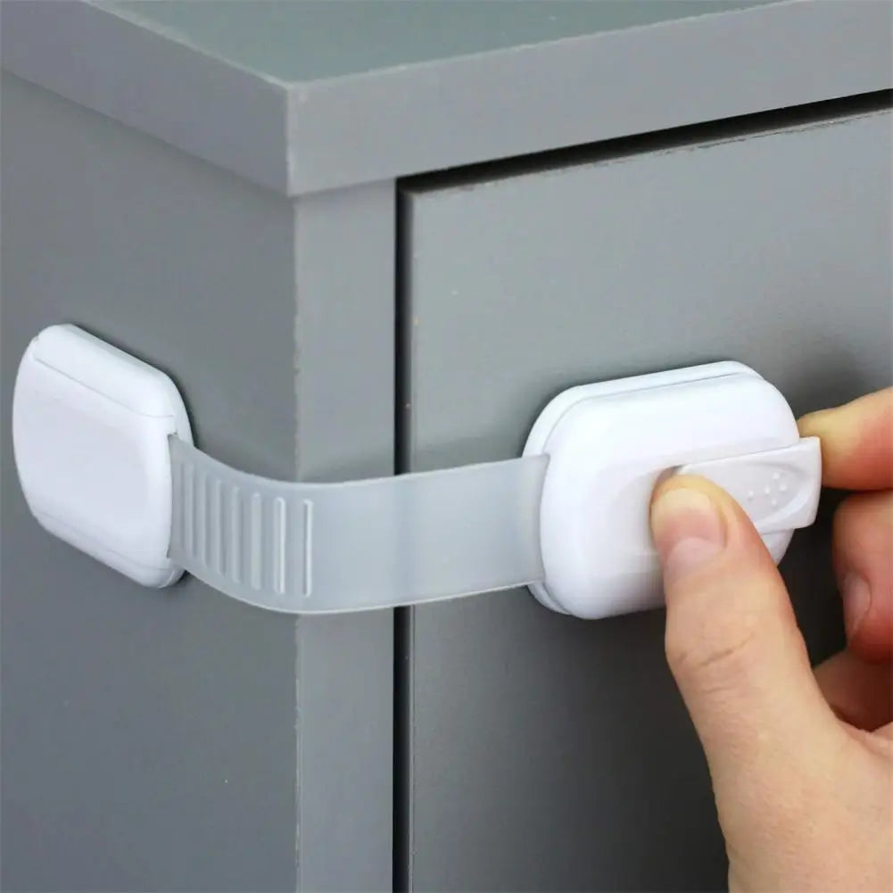 Fingers unlocking a white child safety cabinet latch on a gray cupboard.