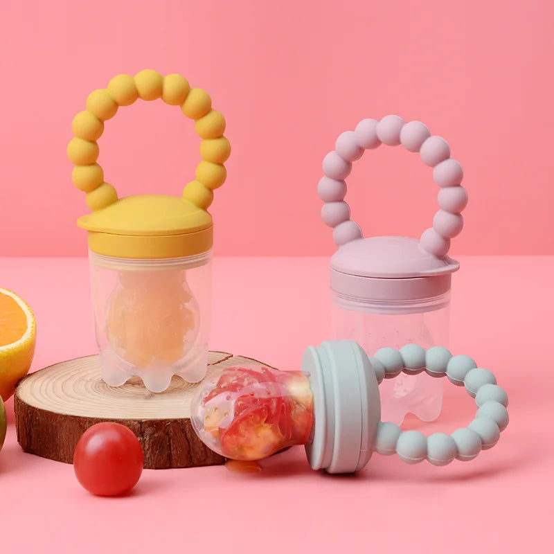 Three colorful baby fruit feeders on a pink background.