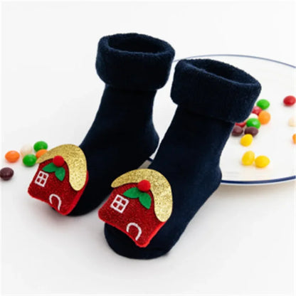 A Pair Of Blue Christmas Baby Socks With Gingerbread House Design With Plates Of Candies In The Background