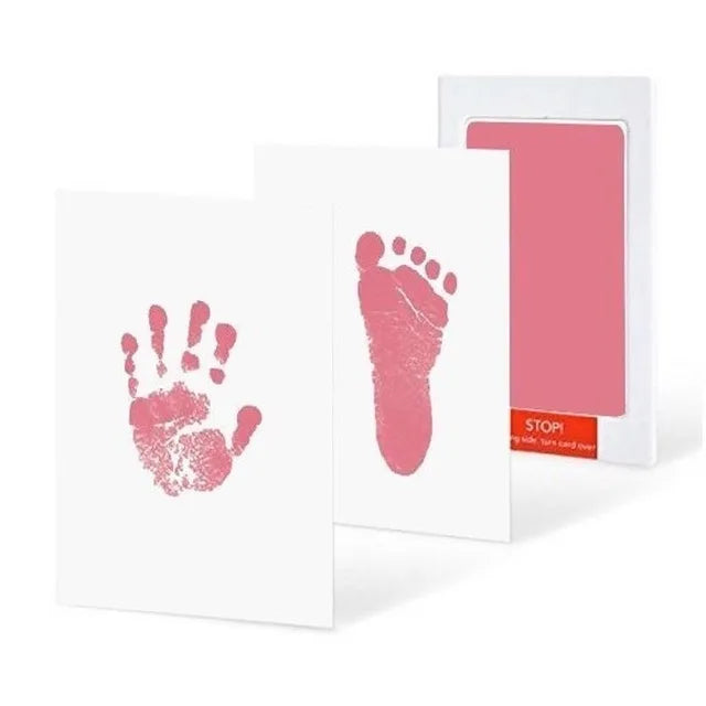 Two cards with pink baby handprint and footprint, next to a pink ink pad and packaging.