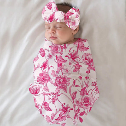 A baby wrapped in a pink floral blanket lying on a bed.