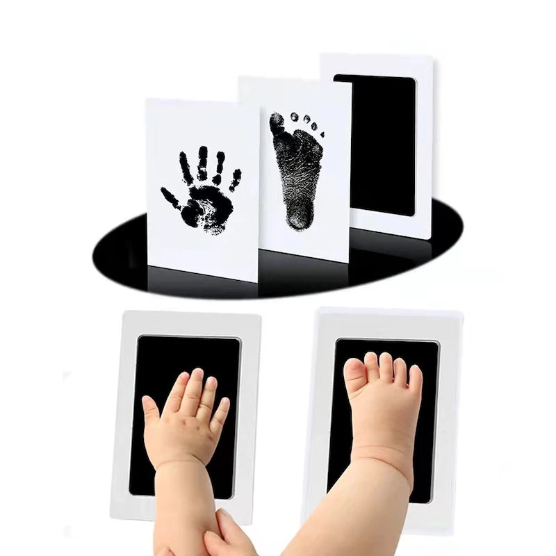 A child's hand and foot being pressed onto ink pads above their corresponding black ink prints.