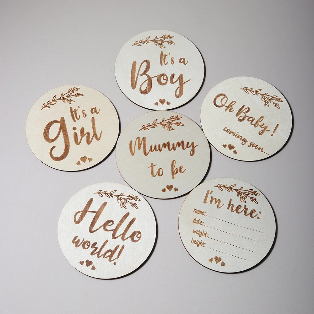 Wooden discs with baby-related phrases like It's a Girl, It's a Boy, and Hello World! on a plain background.