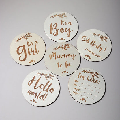 Wooden discs with baby-related phrases like It's a Girl, It's a Boy, and Hello World! on a plain background.