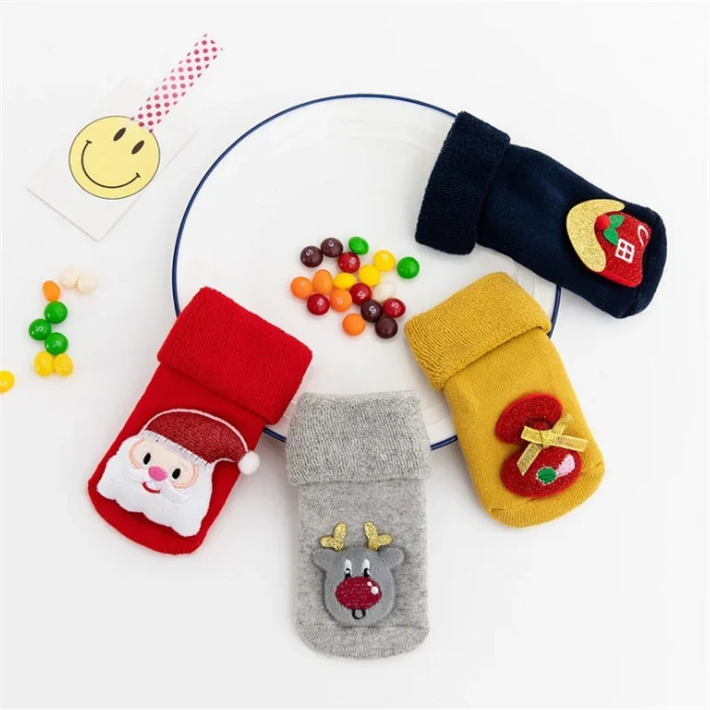 Four Christmas Baby Socks With Cartoon Design In Red, Blue, Yellow, And Grey In A White Background