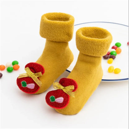 A Pair Of Yellow Christmas Baby Socks With Christmas Bag Design With Plates Of Candies In The Background